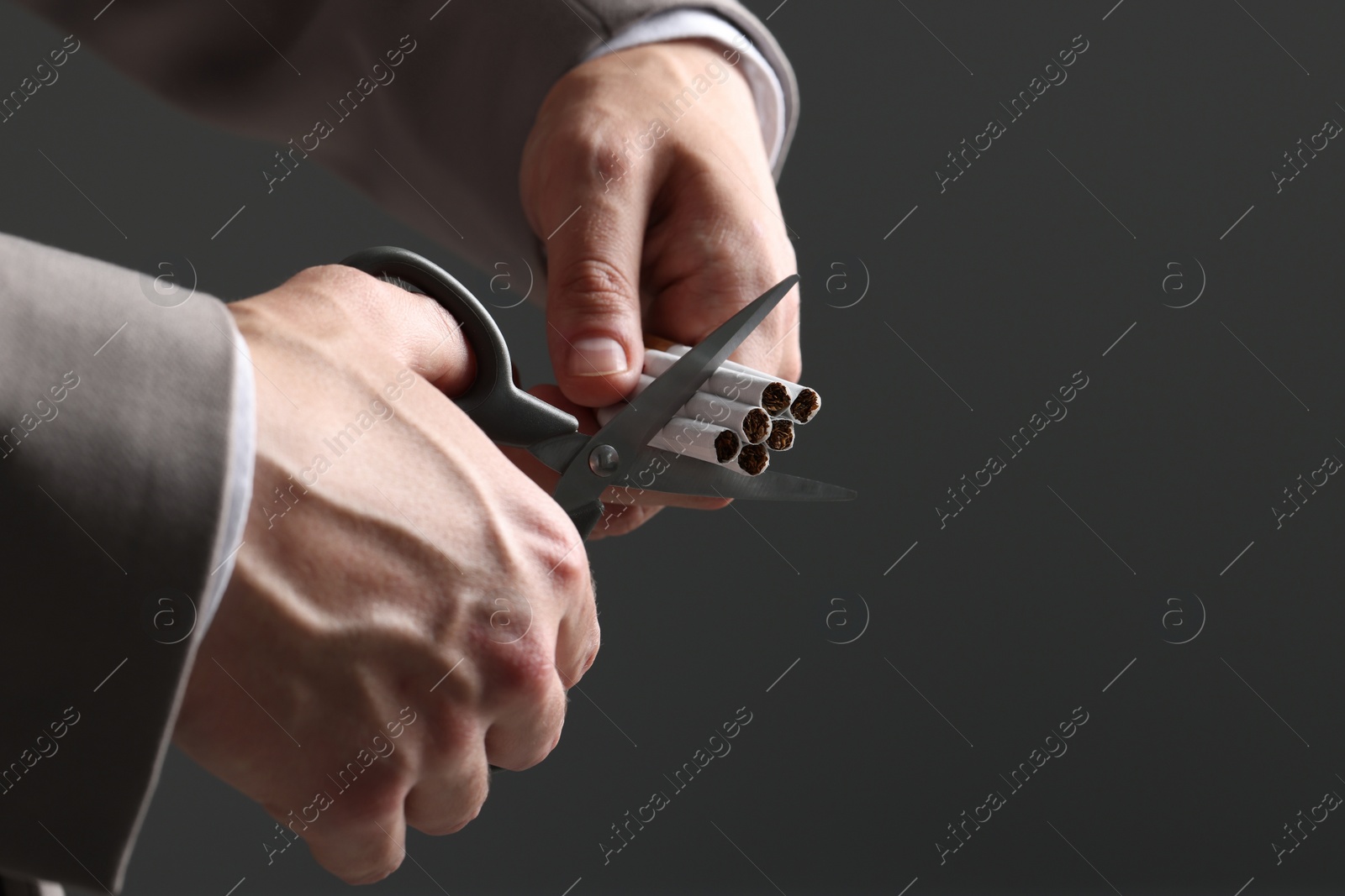 Photo of Stop smoking concept. Man cutting cigarettes on gray background, closeup with space for text