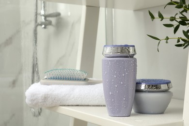 Photo of Hair care cosmetic products, towel and brush on white shelf indoors