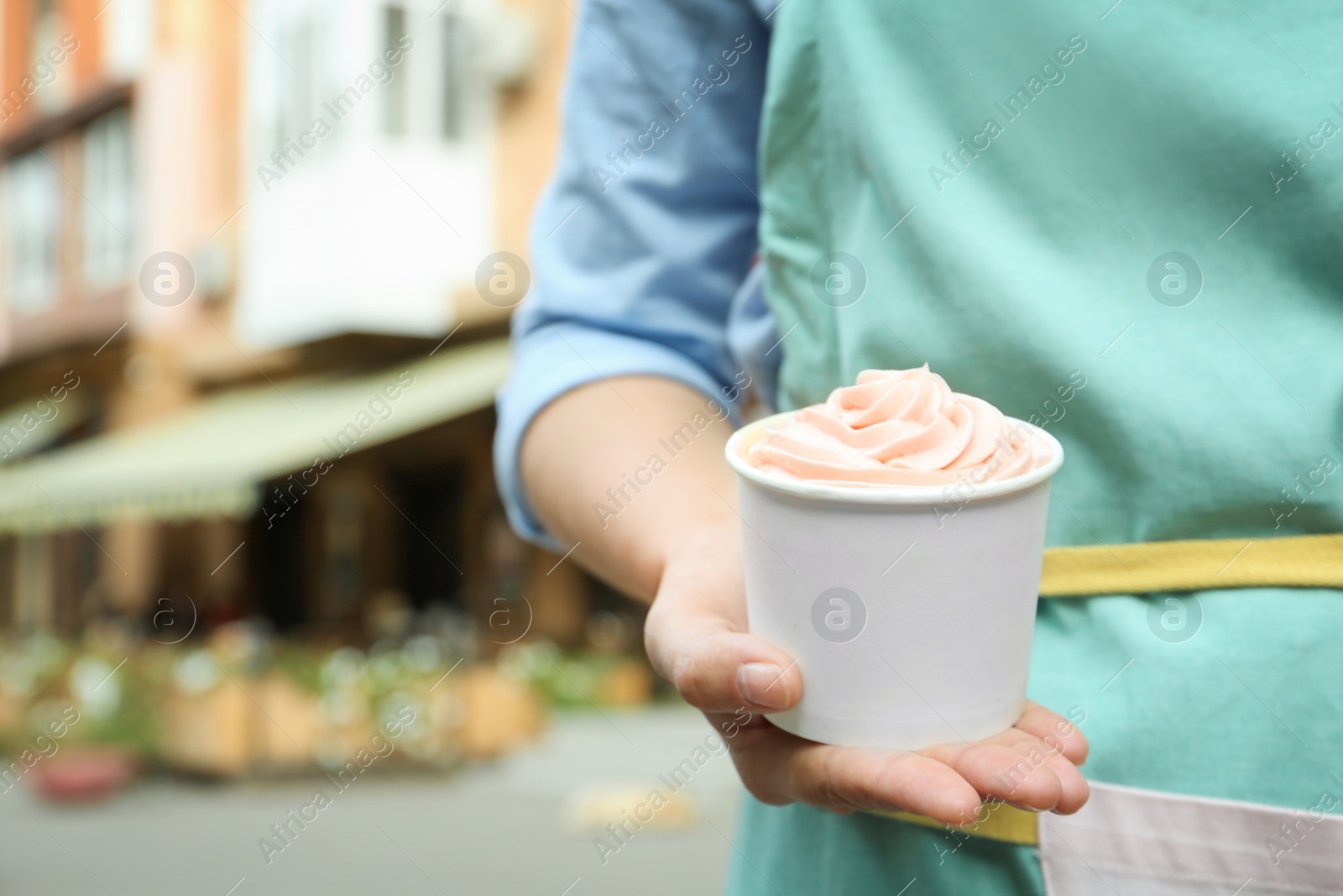 Photo of Woman holding cup with tasty frozen yogurt outdoors, closeup. Space for text