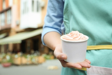 Woman holding cup with tasty frozen yogurt outdoors, closeup. Space for text