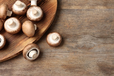 Photo of Fresh champignon mushrooms and cutting board on wooden table, top view with space for text