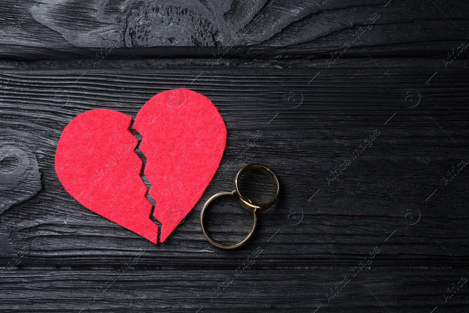 Photo of Divorce concept. Broken red paper heart and wedding rings on black wooden table, flat lay with space for text