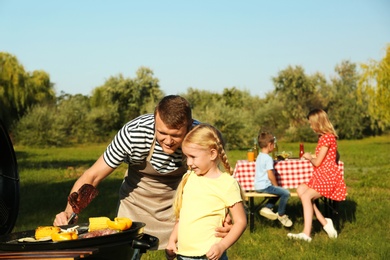 Father with little girl at barbecue grill and their family in park