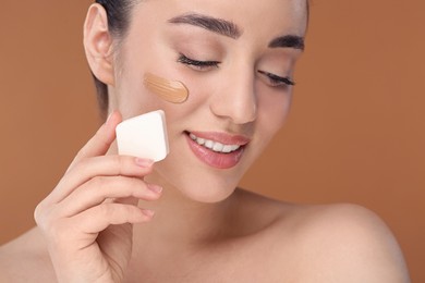 Woman applying foundation on face with makeup sponge against brown background