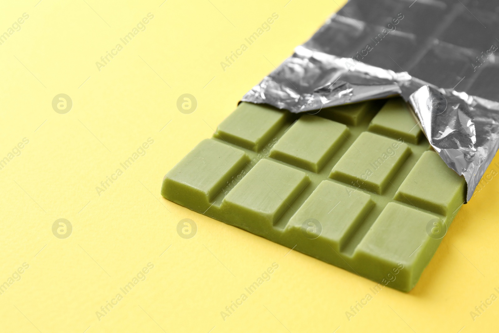 Photo of Tasty matcha chocolate bar wrapped in foil on yellow background, closeup. Space for text