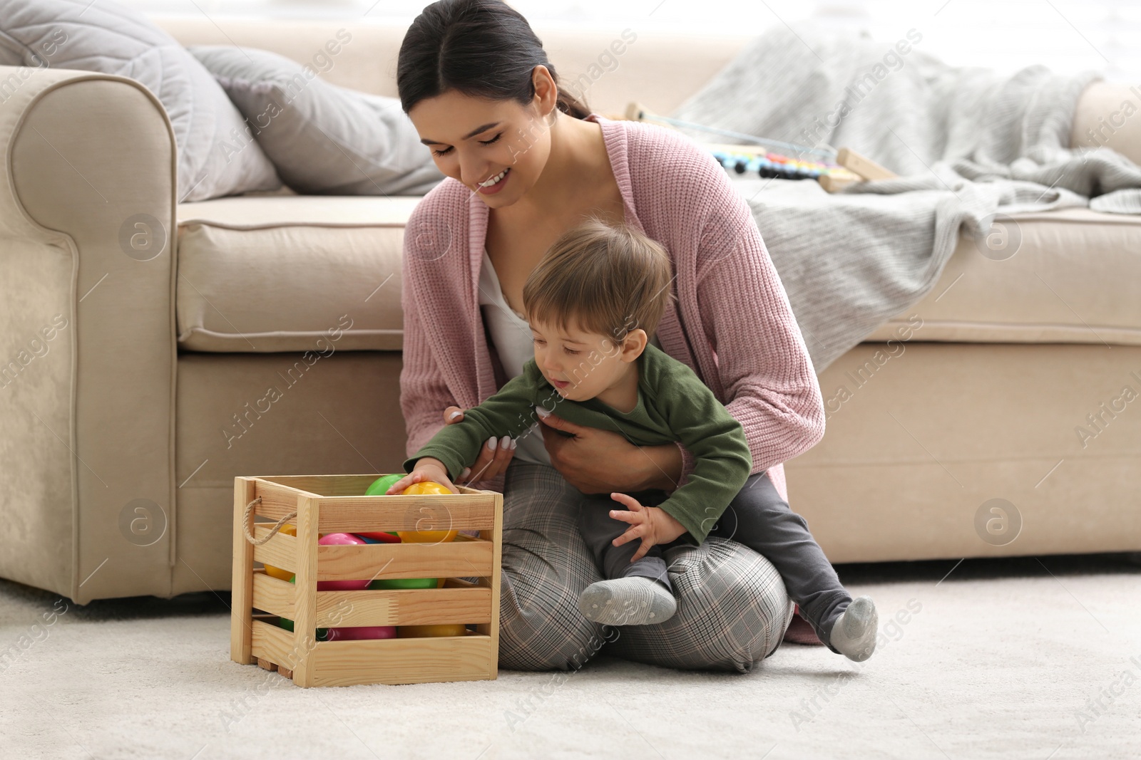 Photo of Young nanny and cute little baby playing with toys at home