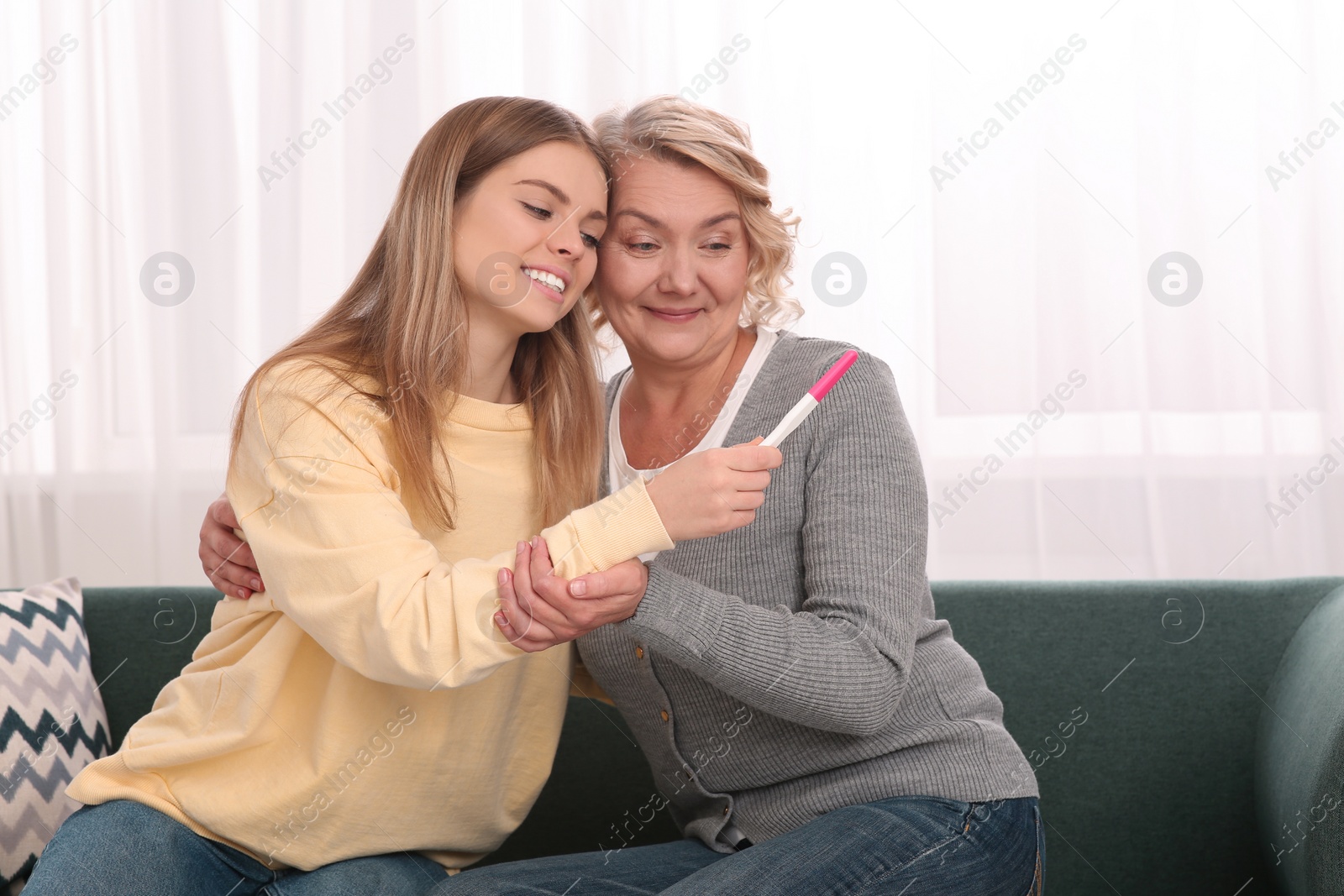 Photo of Young woman showing her mother pregnancy test at home. Grandparent reaction to future grandson