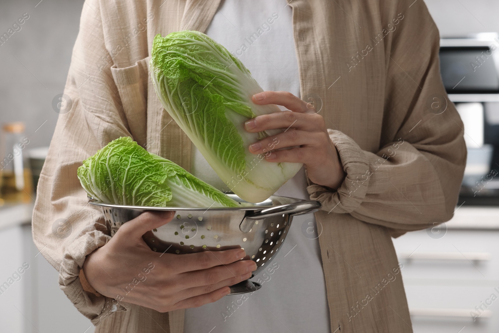 Photo of Woman holding fresh chinese cabbages in kitchen, closeup