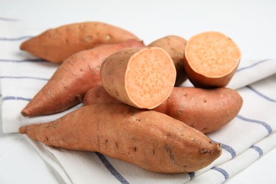 Photo of Whole and cut ripe sweet potatoes on kitchen towel, closeup