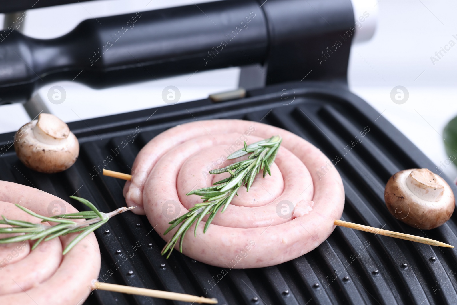 Photo of Homemade sausages, mushrooms and rosemary on electric grill, closeup