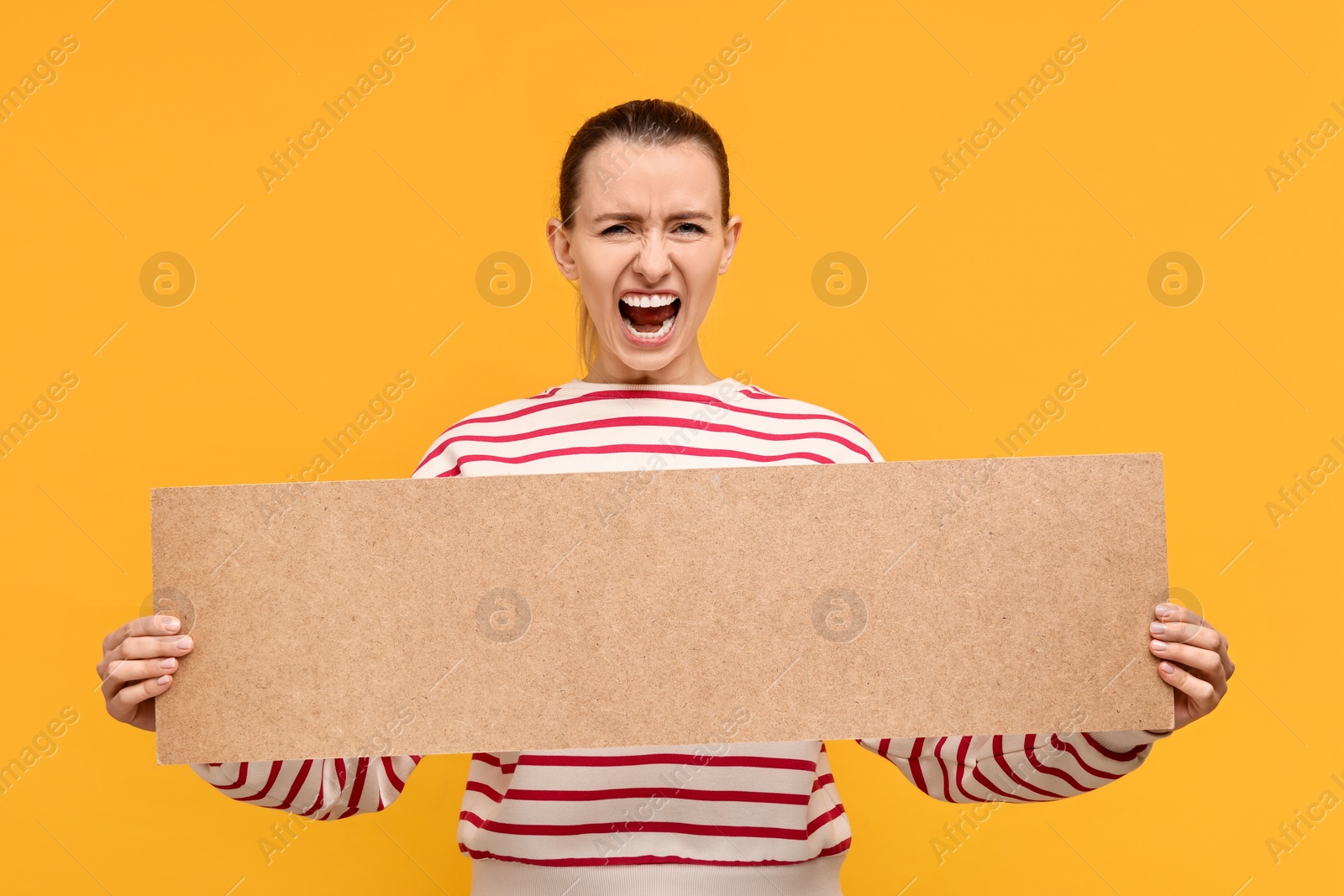 Photo of Screaming woman holding blank cardboard banner on orange background, space for text