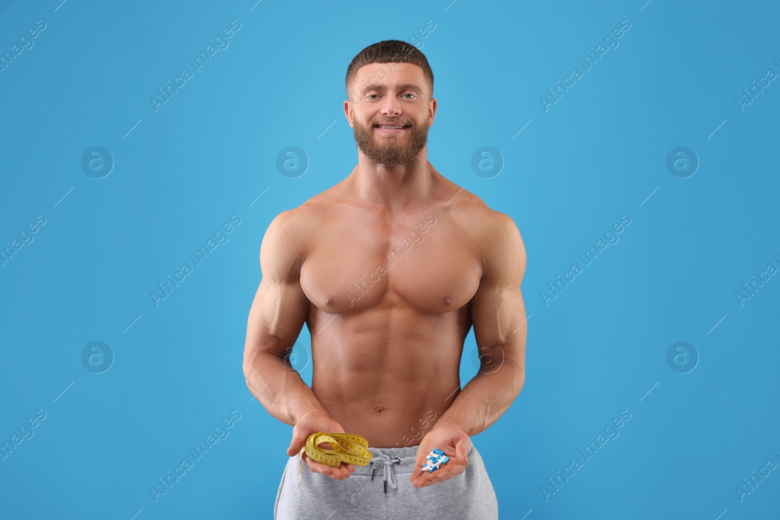 Photo of Athletic young man with measuring tape and pills on light blue background. Weight loss