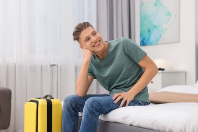 Photo of Smiling guest with suitcase relaxing on bed in stylish hotel room