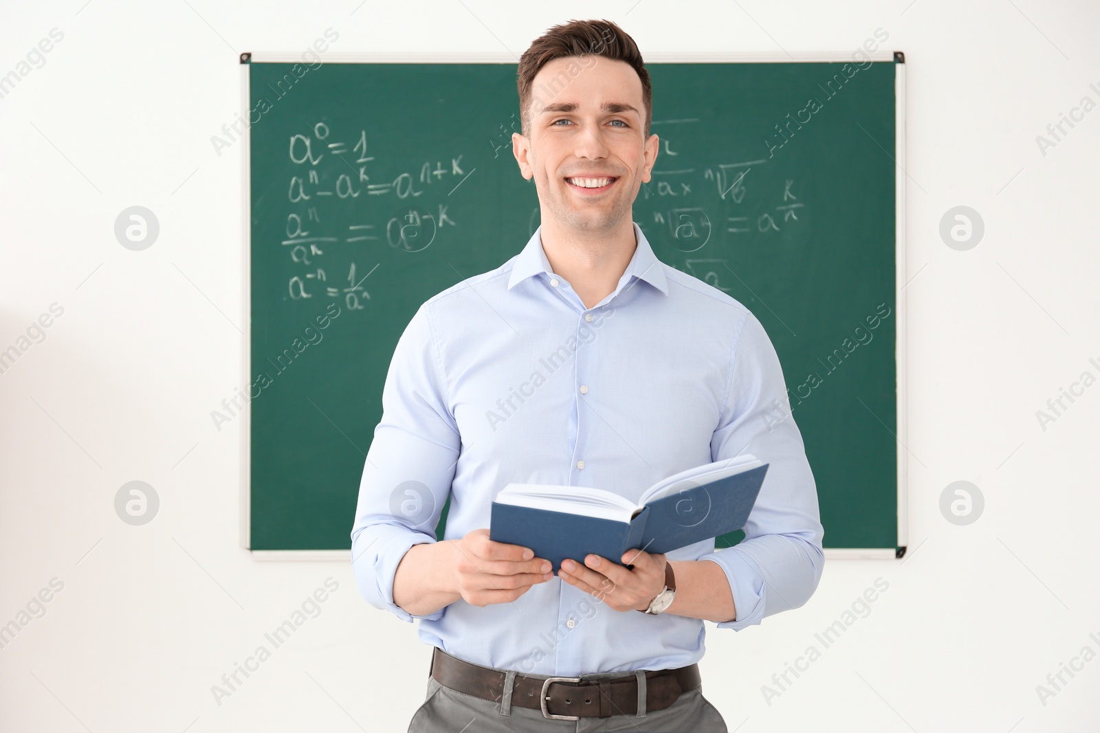 Photo of Young male teacher with book standing in classroom