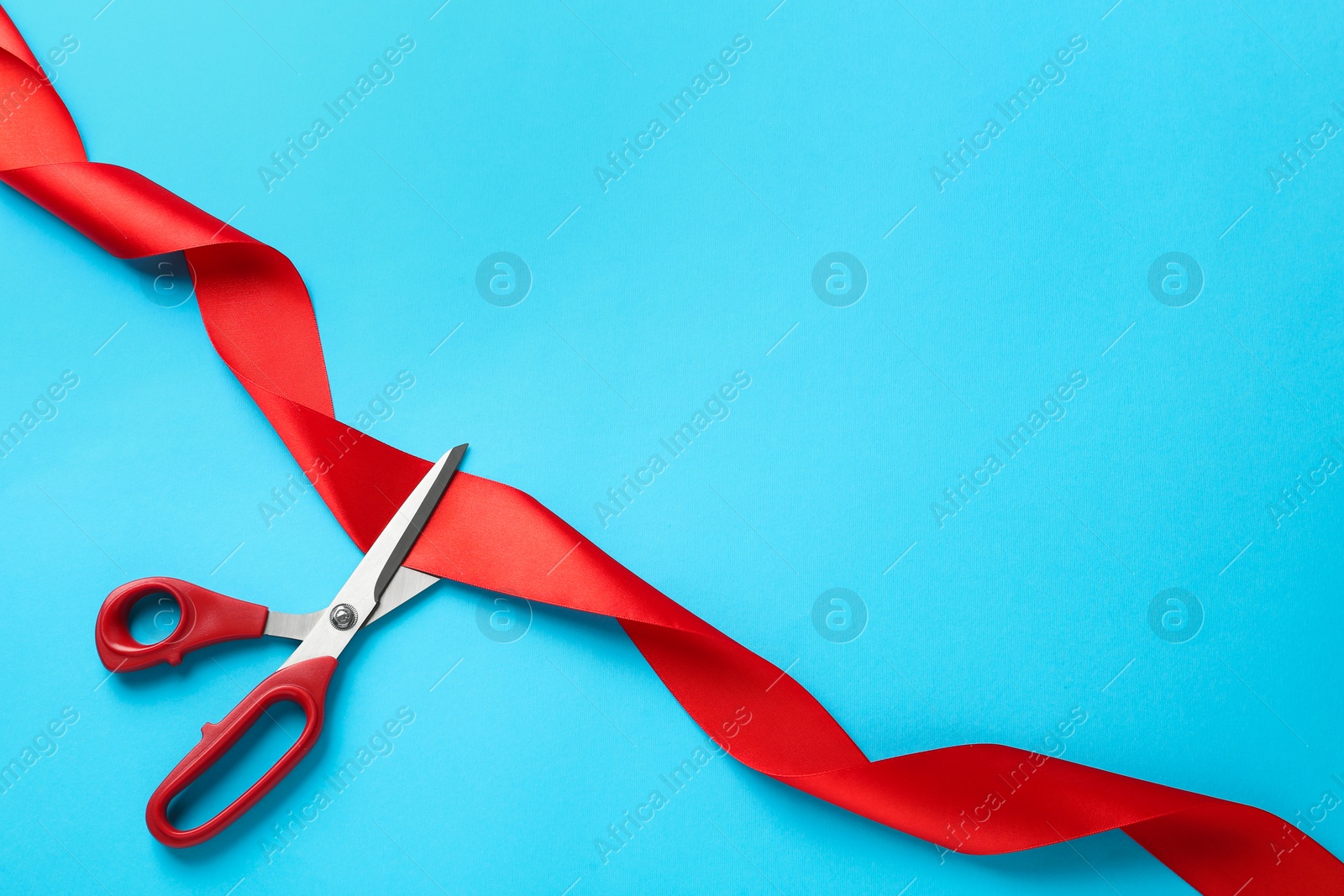 Photo of Red ribbon and scissors on light blue background, top view. Space for text