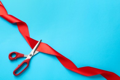 Red ribbon and scissors on light blue background, top view. Space for text