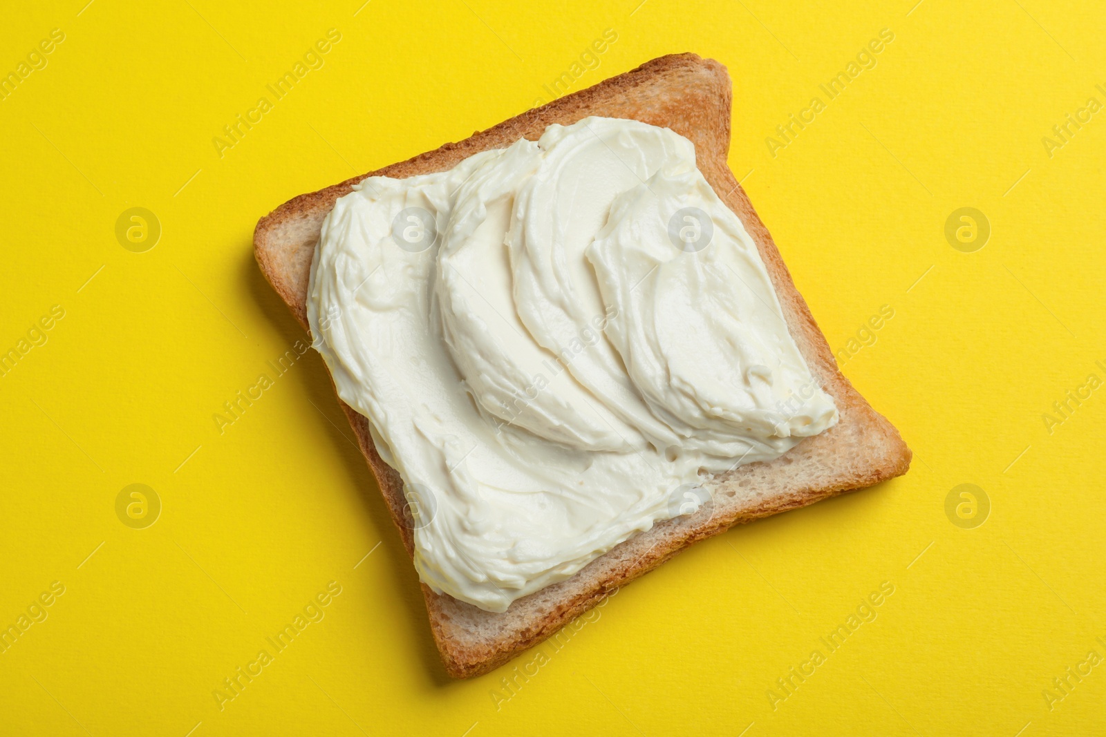 Photo of Slice of bread with tasty cream cheese on yellow background, top view