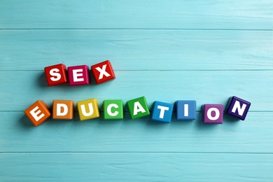 Photo of Colorful wooden blocks with phrase "SEX EDUCATION" on light blue background, flat lay