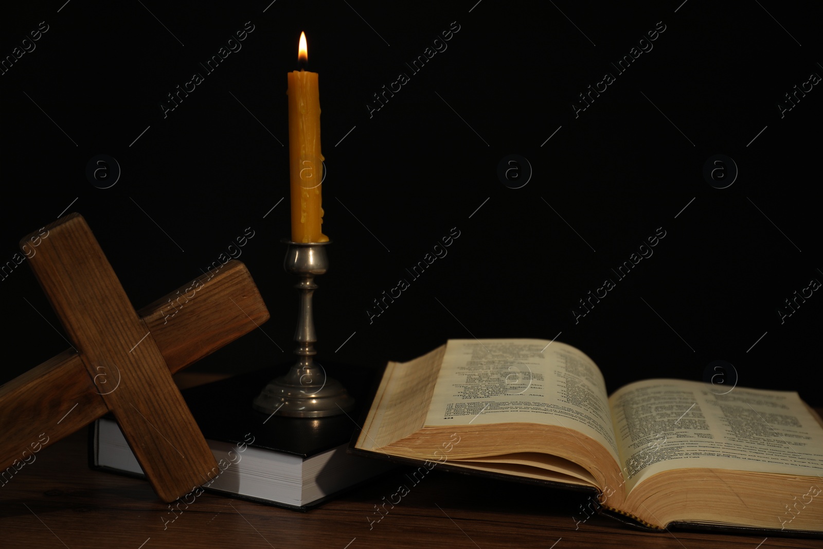 Photo of Church candle, Bible and cross on wooden table against black background