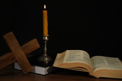 Photo of Church candle, Bible and cross on wooden table against black background