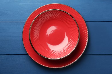Photo of Beautiful red ceramic plate and bowl on blue wooden table, top view