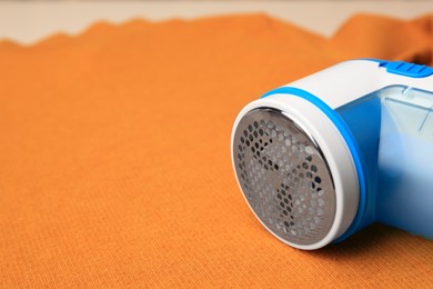 Photo of Modern fabric shaver on orange cloth with lint, closeup. Space for text