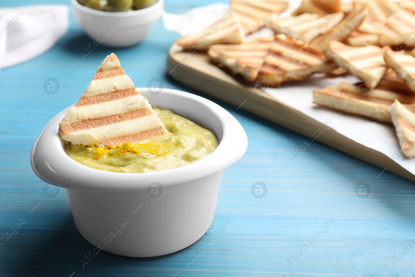 Photo of Delicious pita chips and hummus on light blue wooden table, closeup
