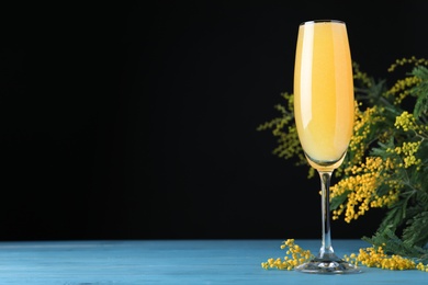 Photo of Glass of Mimosa cocktail with flowering branches on light blue wooden table. Space for text