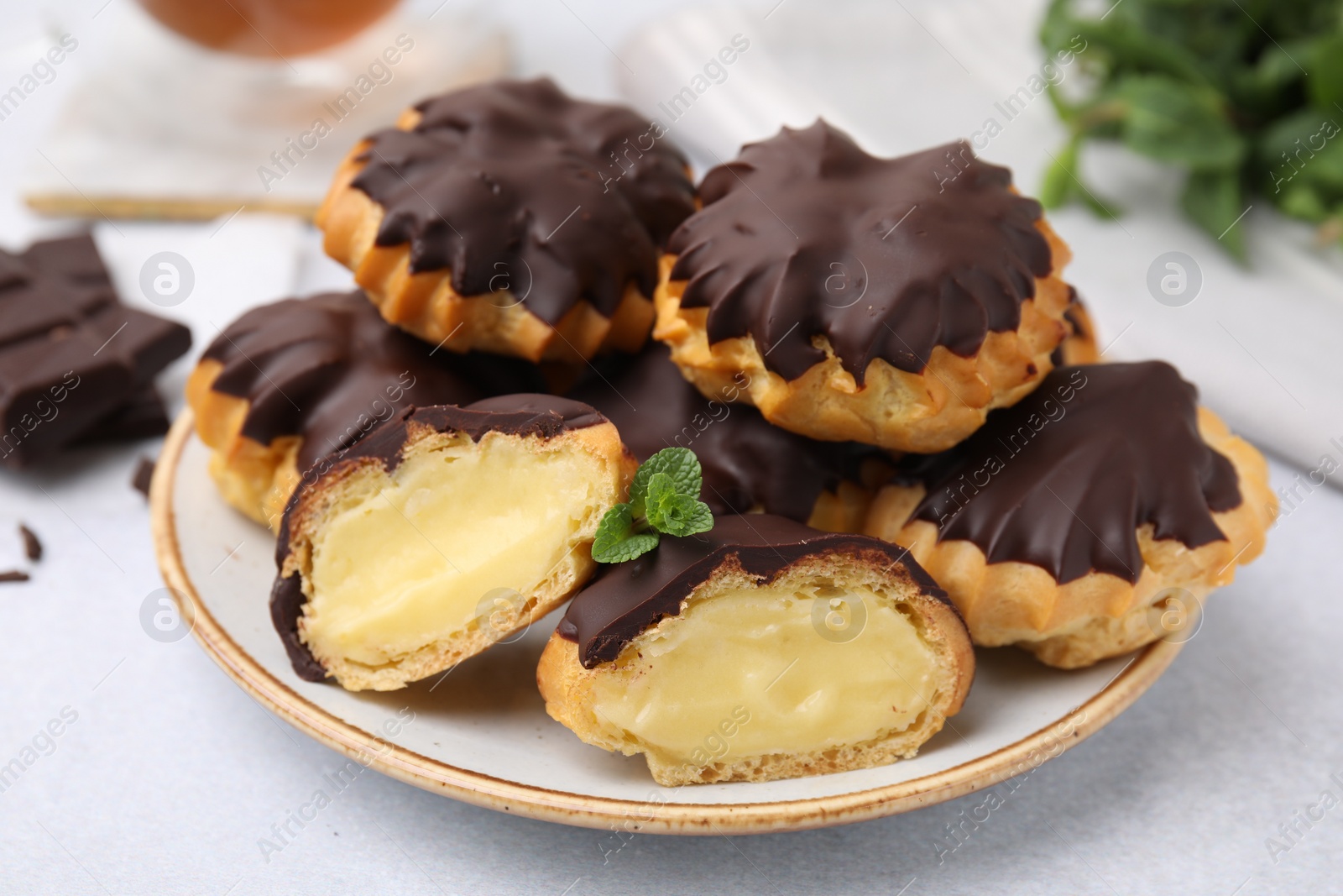 Photo of Delicious profiteroles with chocolate spread and cream on white table, closeup