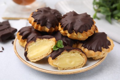 Photo of Delicious profiteroles with chocolate spread and cream on white table, closeup