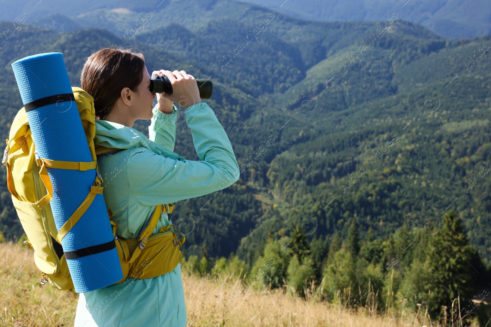 Photo of Tourist with hiking equipment looking through binoculars in mountains