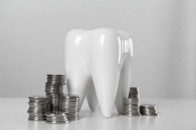 Photo of Ceramic model of tooth and coins on white table. Expensive treatment
