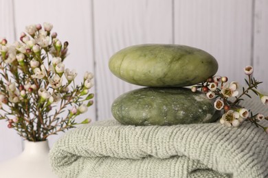 Photo of Composition with spa stones on towel and flowers against wooden background, closeup