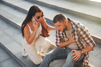 Woman calling ambulance to help man with heart attack on stairs