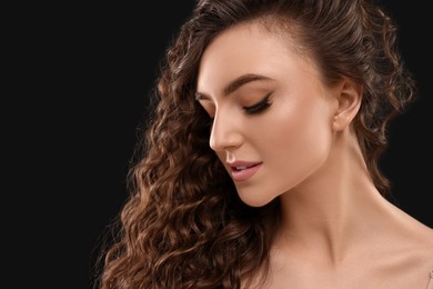 Photo of Beautiful young woman with long curly brown hair on black background, closeup. Space for text