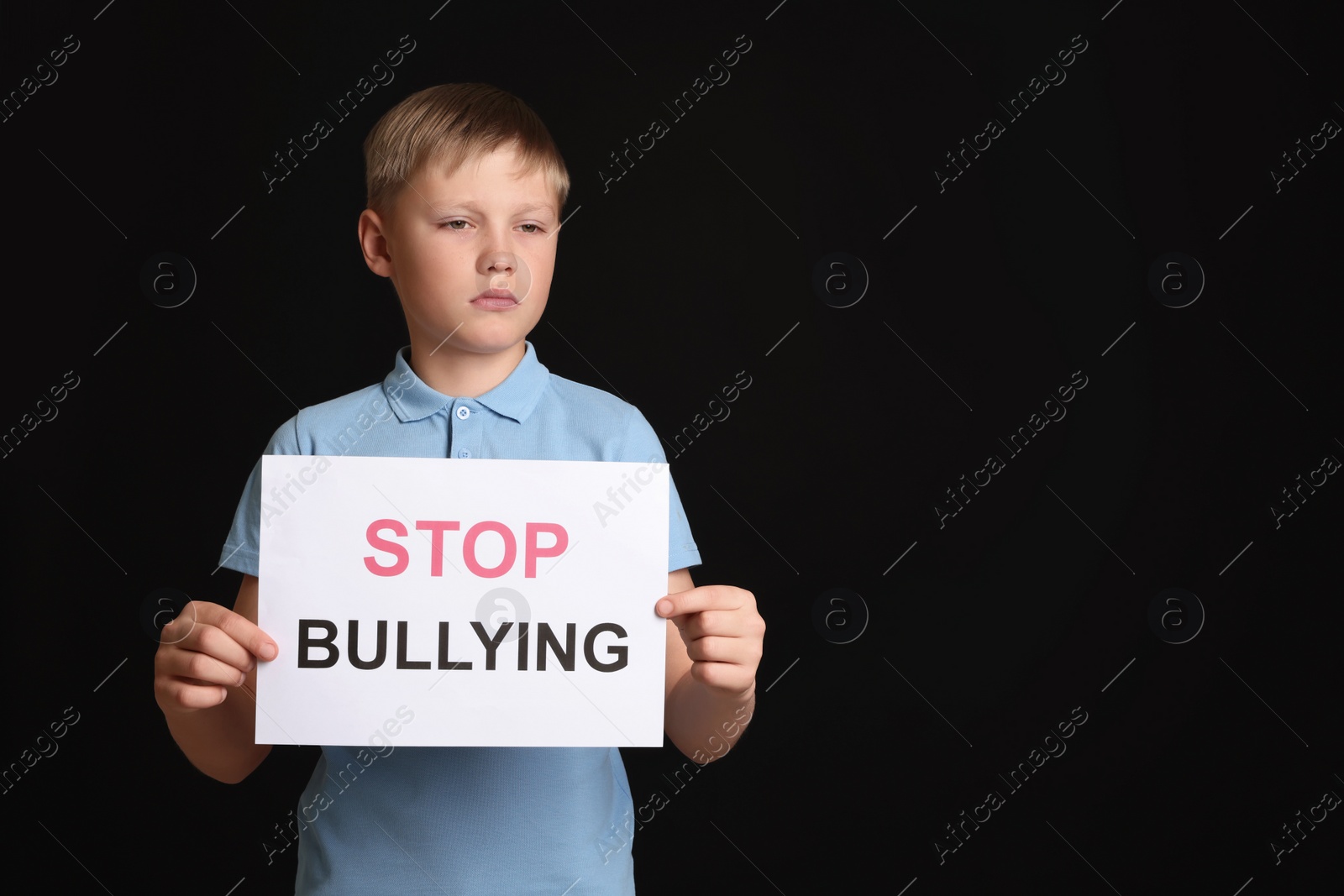 Photo of Boy holding sign with phrase Stop Bullying on black background, space for text