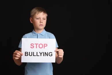Boy holding sign with phrase Stop Bullying on black background, space for text