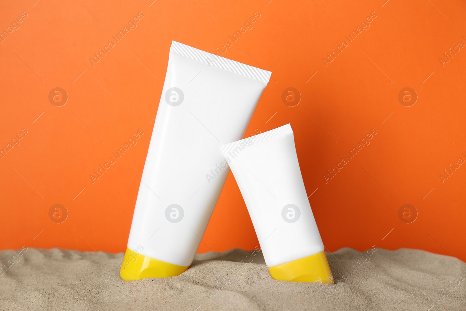 Photo of Different suntan products on sand against orange background