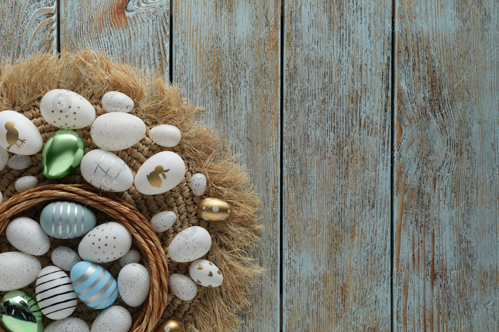 Photo of Decorative nest and many beautiful Easter eggs on wooden table, flat lay. Space for text