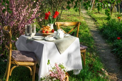 Photo of Beautiful bouquet of tulips and freshly baked waffles on table served for tea drinking in garden