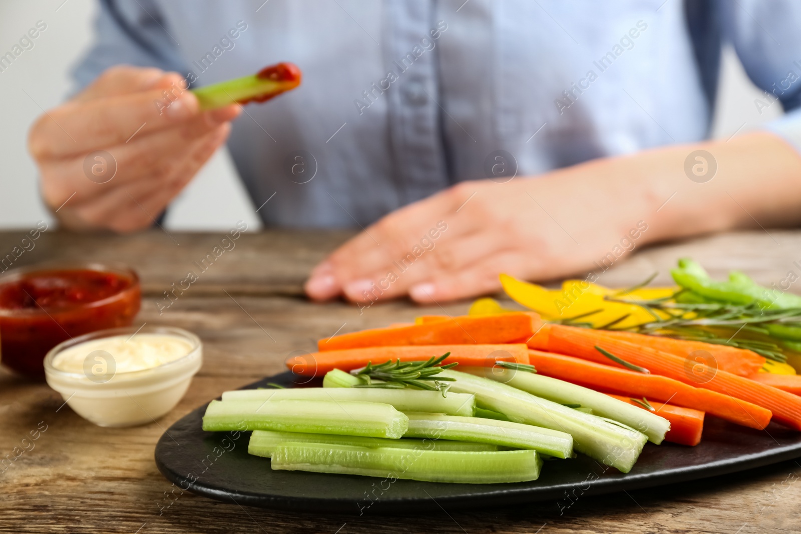 Photo of Plate with celery sticks, other vegetables and different dip sauces on wooden table, closeup