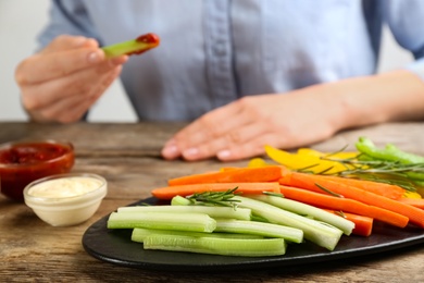 Photo of Plate with celery sticks, other vegetables and different dip sauces on wooden table, closeup