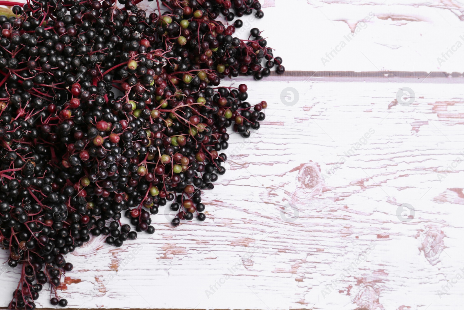 Photo of Pile of tasty elderberries (Sambucus) on white wooden table, top view. Space for text