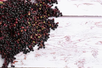 Pile of tasty elderberries (Sambucus) on white wooden table, top view. Space for text