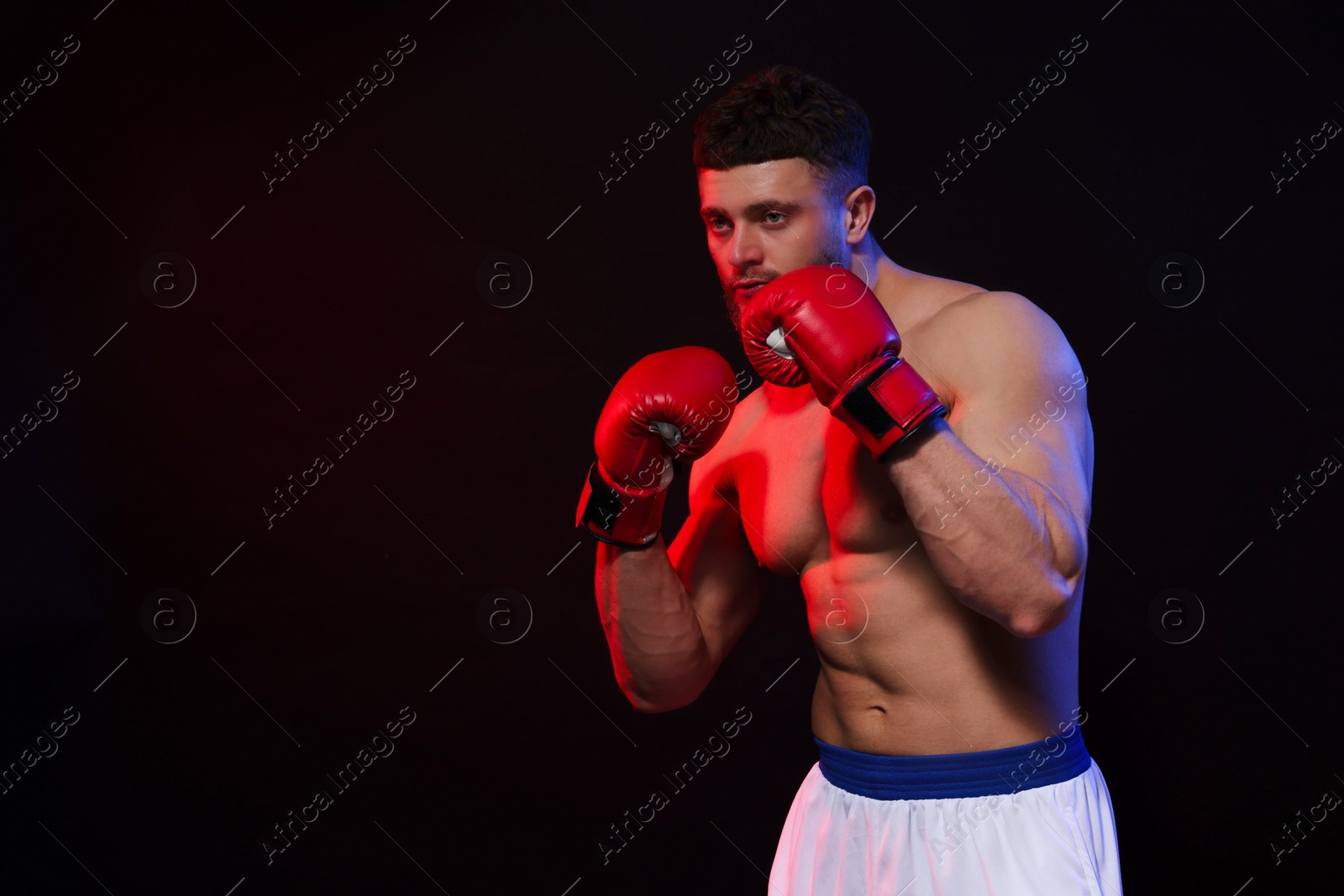 Photo of Man wearing boxing gloves on dark background. Space for text