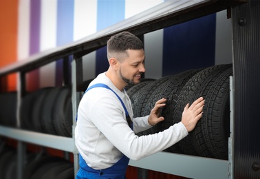 Mechanic near rack with car tires at service station