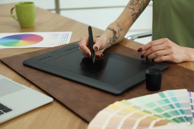 Professional designer with graphic tablet at wooden table, closeup