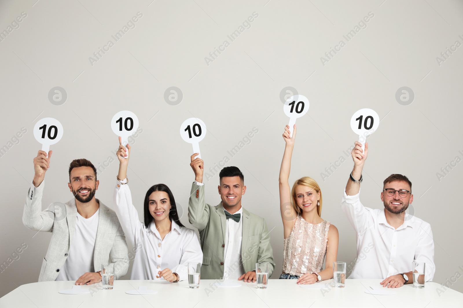 Photo of Panel of judges holding signs with highest score at table on beige background