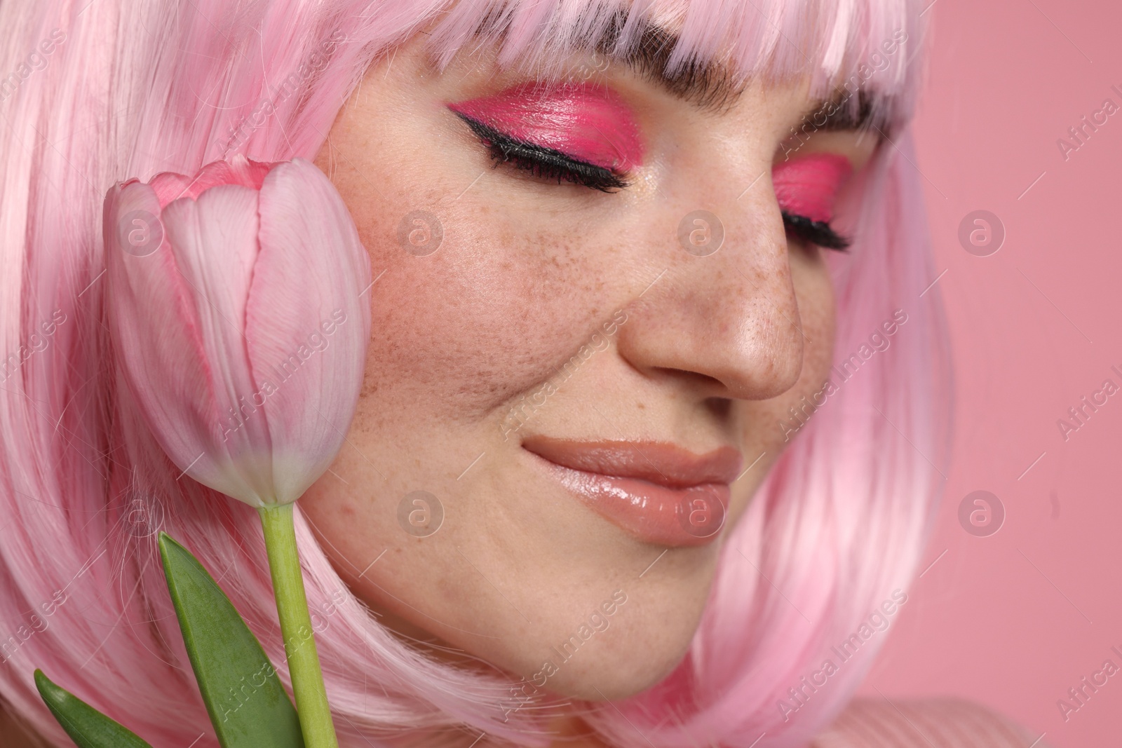 Photo of Beautiful woman with bright makeup, fake freckles and tulip on pink background, closeup