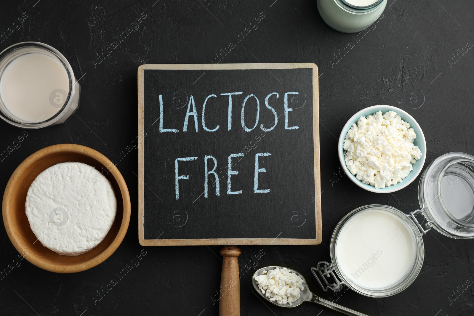 Photo of Dairy products and board with phrase Lactose free on black textured table, flat lay